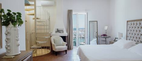 A hotel room with a bed, a chair, a small table, a balcony with a view, and a staircase.