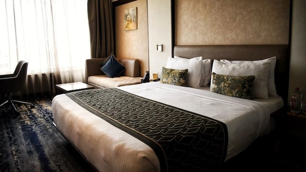 A hotel room with a large bed, a sofa, a small table, and a chair. - Sayaji Vadodara (Vadodara)