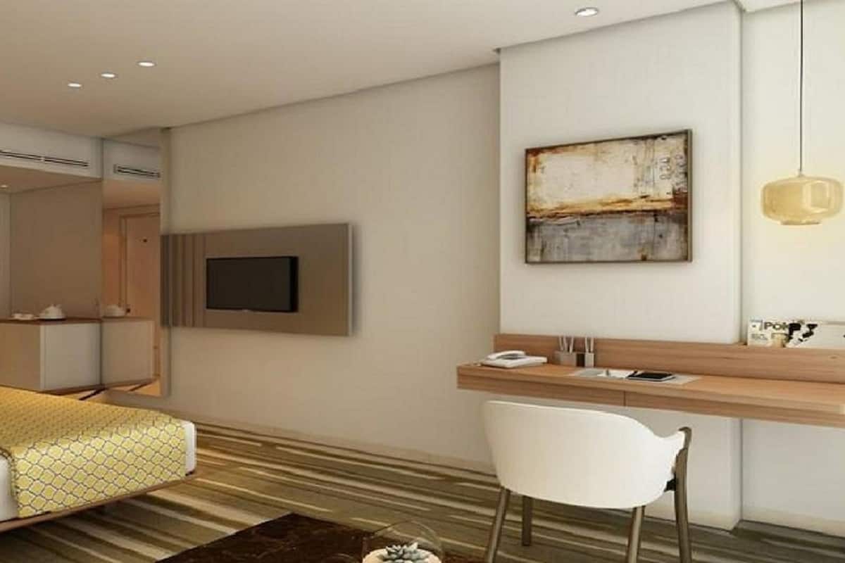 A modern hotel room with a bed, a desk, a chair, a television, and a painting on the wall.