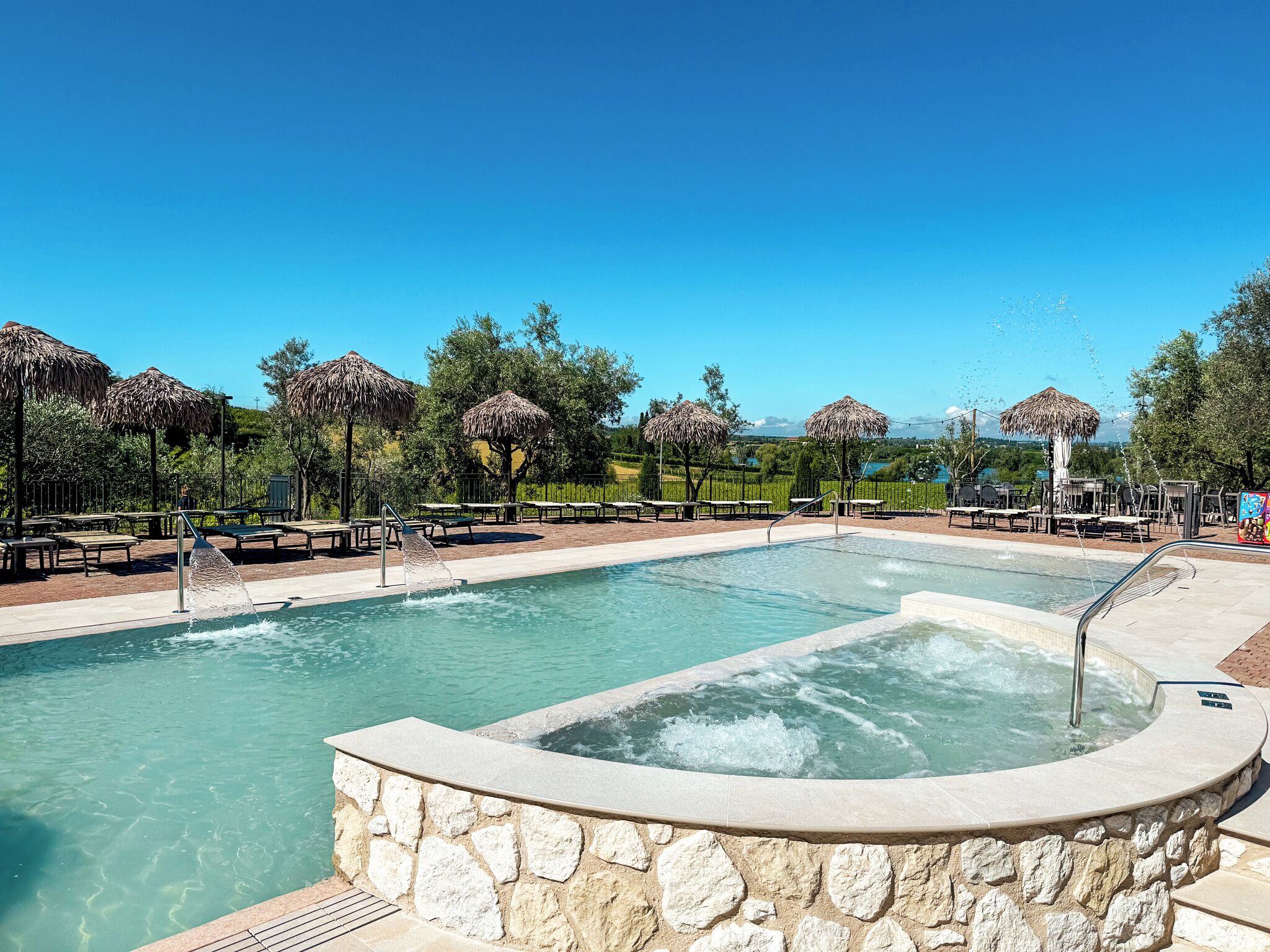 A swimming pool with a hot tub, lounge chairs, and thatched umbrellas.