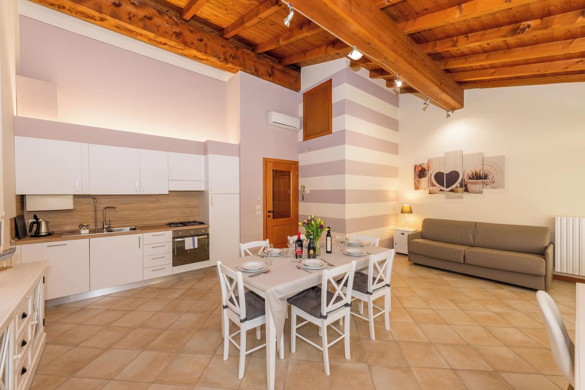 Une cuisine moderne avec des meubles blancs, une table à manger pour quatre personnes et un canapé dans l’espace salon.