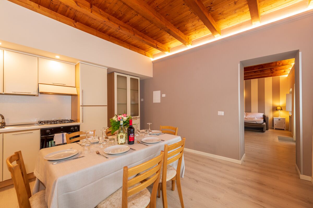 Un coin repas avec une table dressée pour quatre personnes, des chaises en bois, une cuisine équipée d’armoires et un plafond en bois.