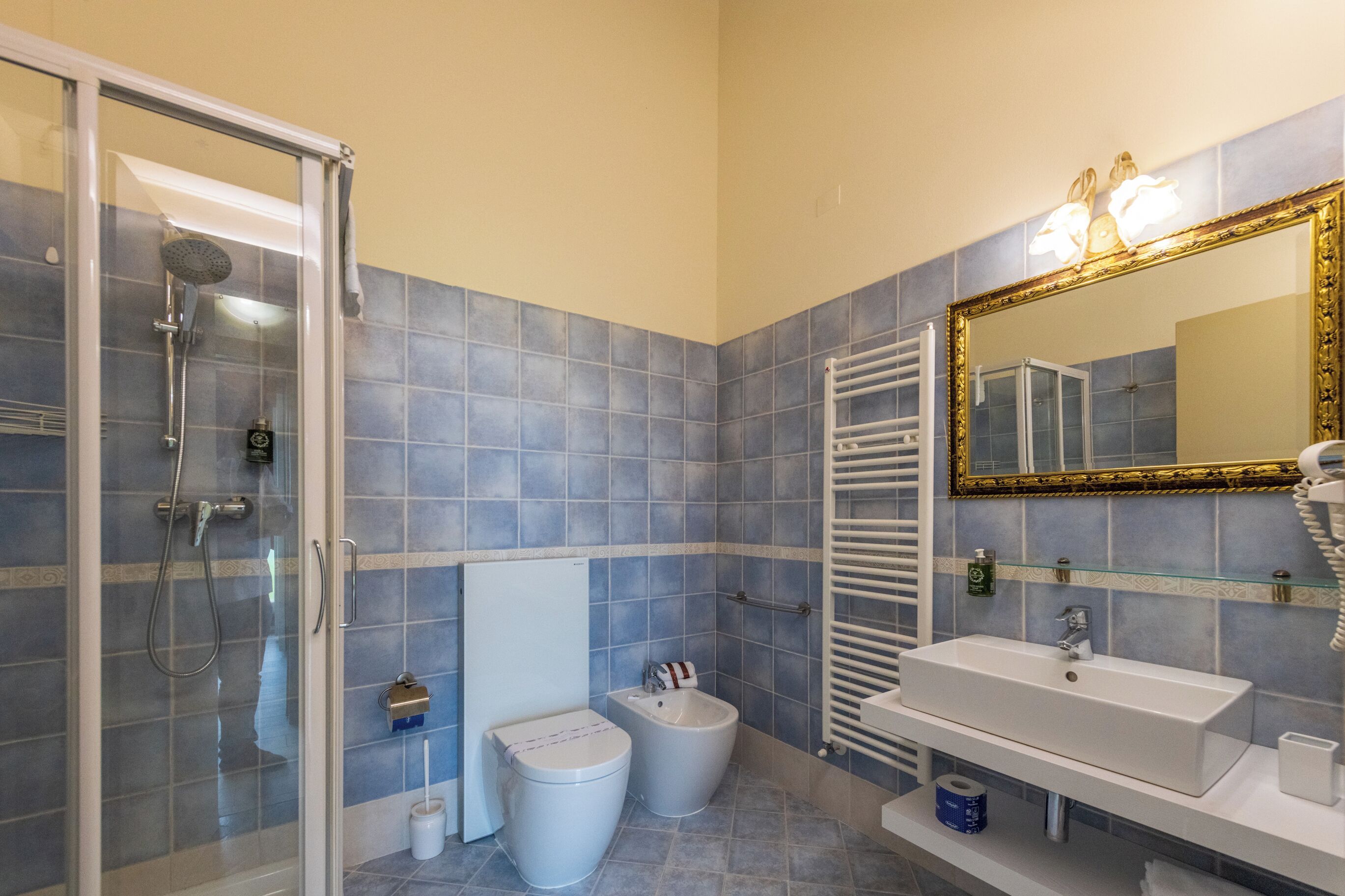 A bathroom with a glass-enclosed shower, a white sink, and a large mirror with a gold frame.