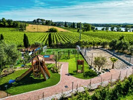 Un parque infantil con toboganes y columpios, un campo de fútbol y una cancha de tenis rodeados de viñedos.