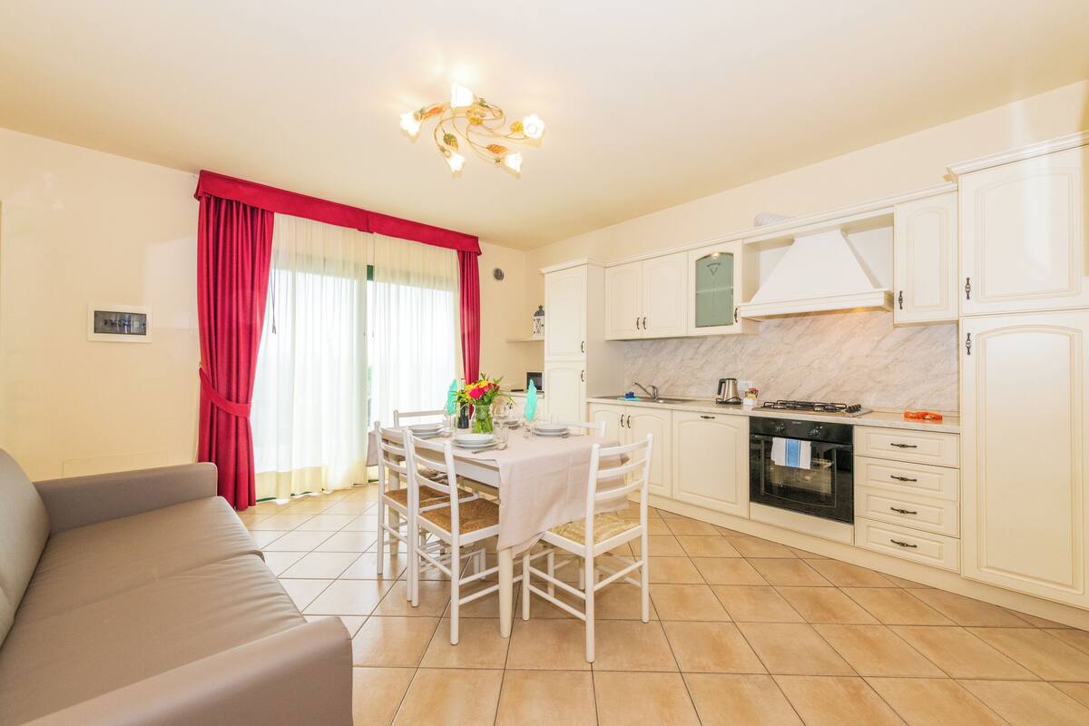 Une cuisine moderne avec des meubles blancs, une table à manger dressée pour quatre personnes et un rideau rouge.