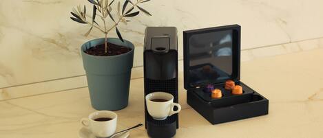 A coffee maker, a cup of coffee, a small plant, and a box of cookies on a marble surface.