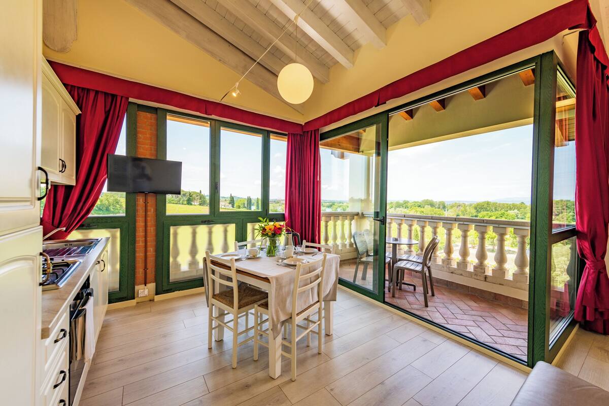 Un coin repas avec une table dressée pour quatre personnes, de grandes fenêtres et une vue sur la verdure environnante.