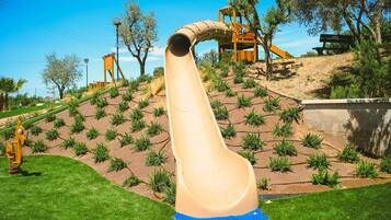 A playground with a slide, climbing area, and a wooden structure.