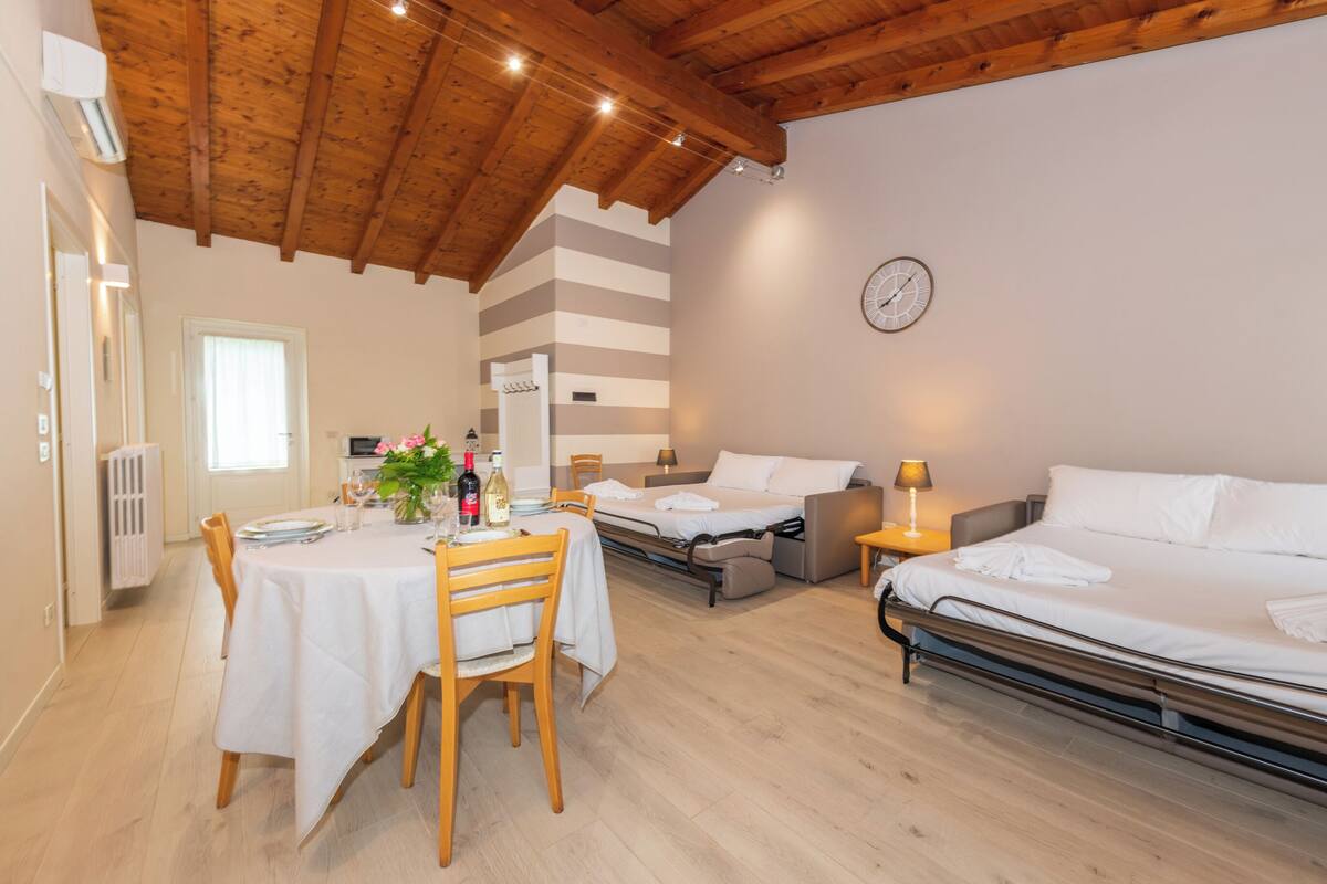 Une chambre d’hôtel avec un plafond en bois, une table à manger avec des chaises, un lit et une table de chevet avec une lampe.