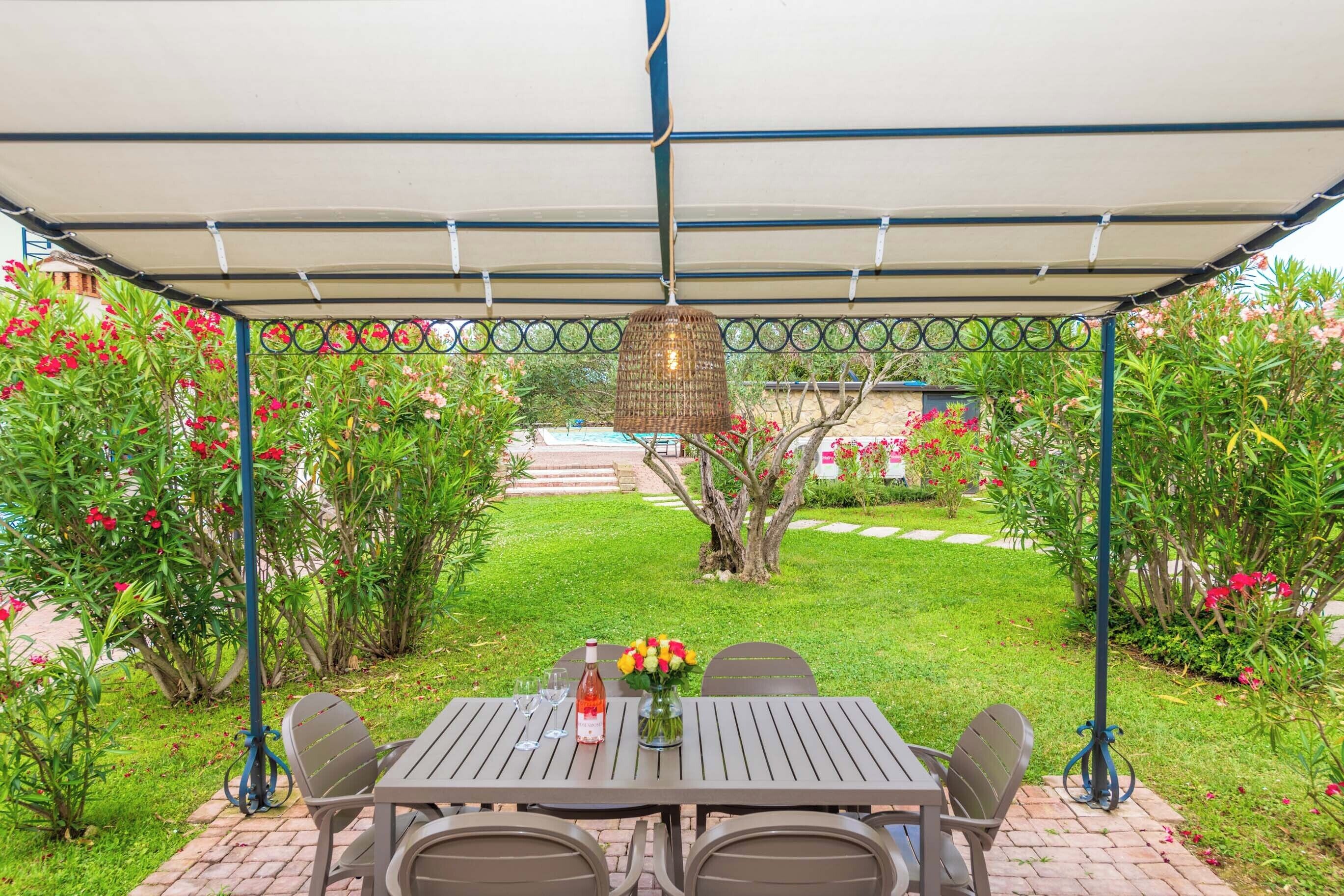 A covered patio with a table set for two, surrounded by lush greenery and flowering plants.