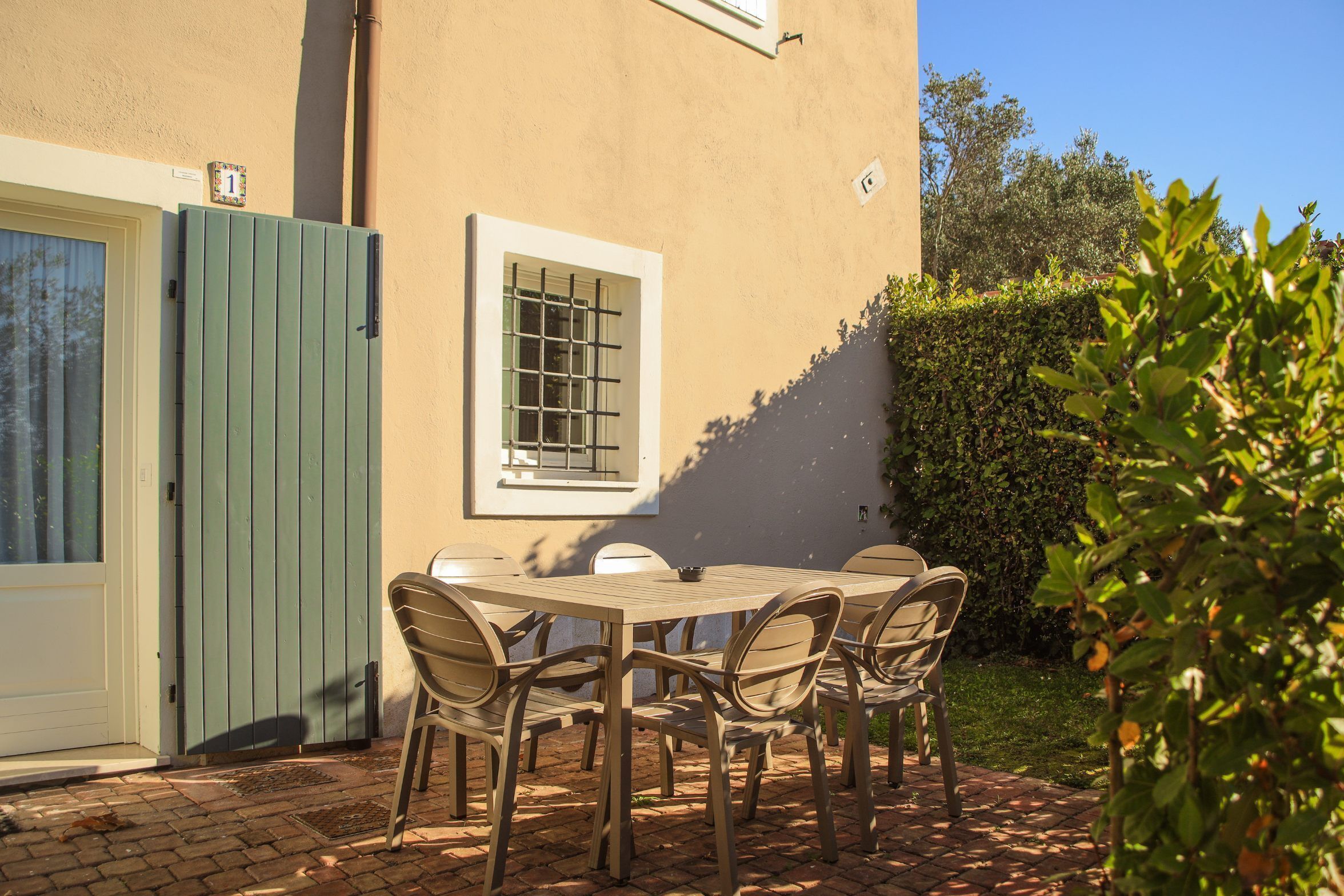 Une terrasse avec une table et des chaises, un portail vert et une fenêtre avec des barreaux.