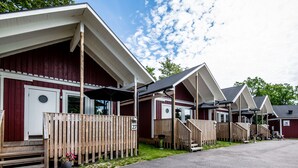 A row of wooden cabins with white trim, each featuring a porch and a door with a circular window. - Dragsö Camping & Stugby (Karlskrona)