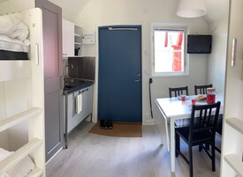 Cocina compacta con lavabo, estufa y una puerta azul. Hay una mesa de comedor con sillas y un televisor montado en la pared.