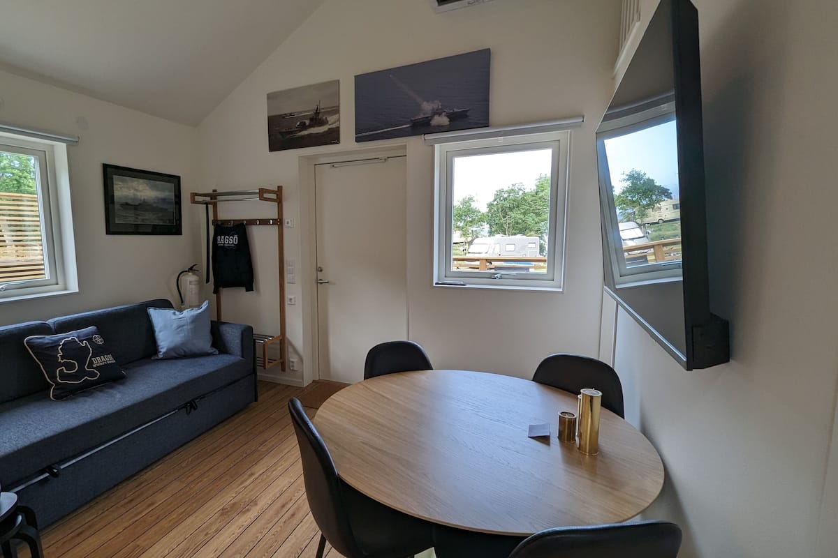 A cozy living area with a sofa, a round table, and two windows.