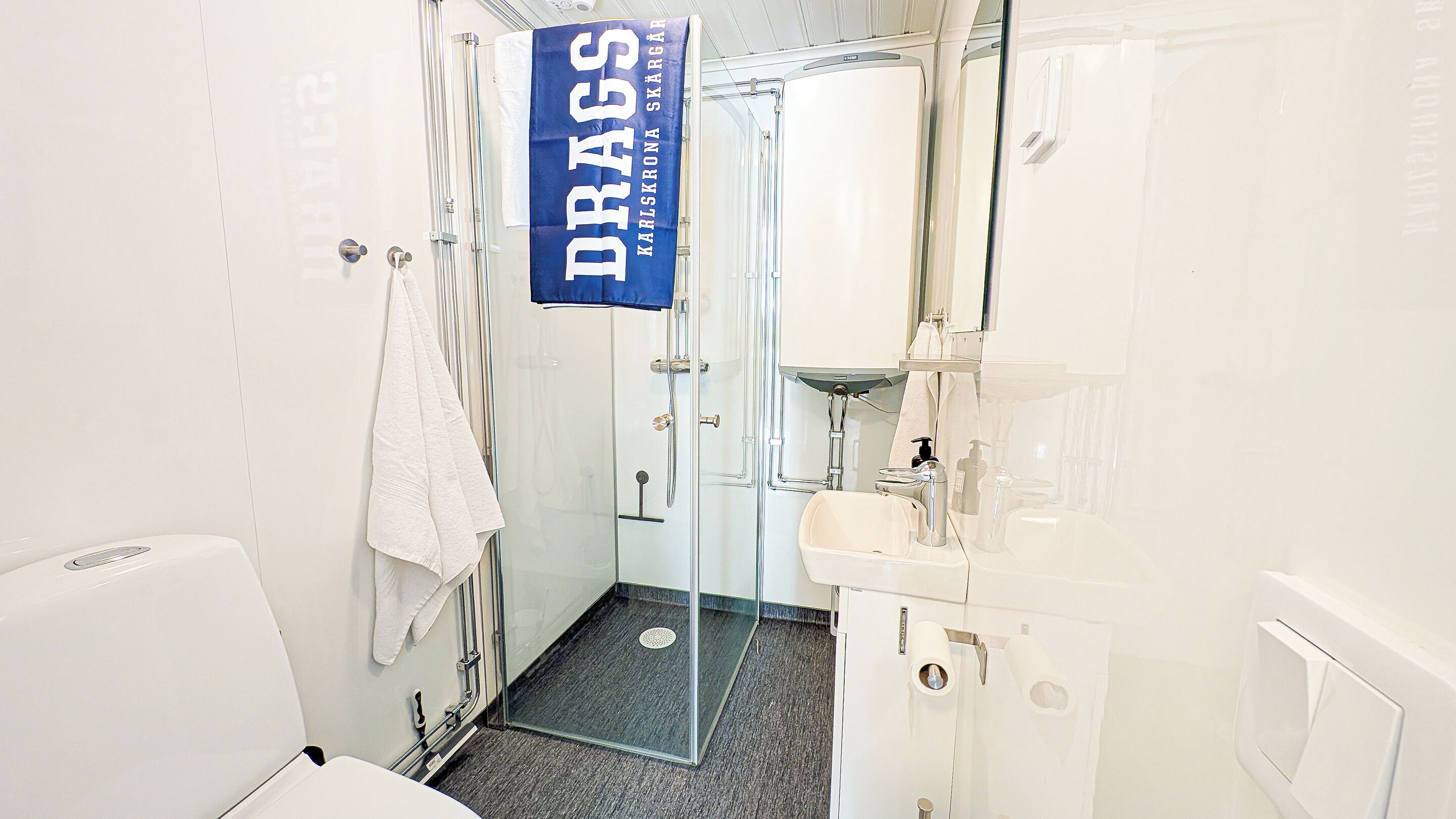 Een badkamer met een douchecabine van glas, een witte wastafel en een handdoek aan de muur.