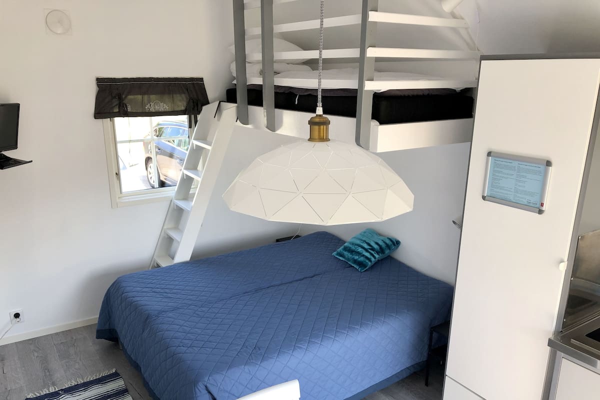 A bedroom with a bunk bed, a desk, a chair, a window with a view, and a hanging light fixture.