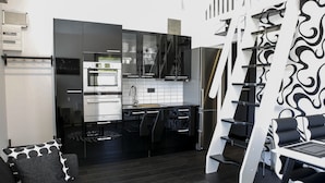 A modern kitchen with black and white appliances, a dining area with a black and white patterned table, and a black sofa with patterned cushions. - Dragsö Camping & Stugby (Karlskrona)
