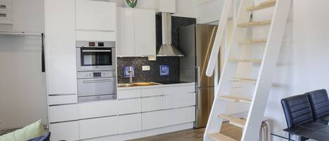 A modern kitchen with white cabinetry, stainless steel appliances, and a wooden dining table.