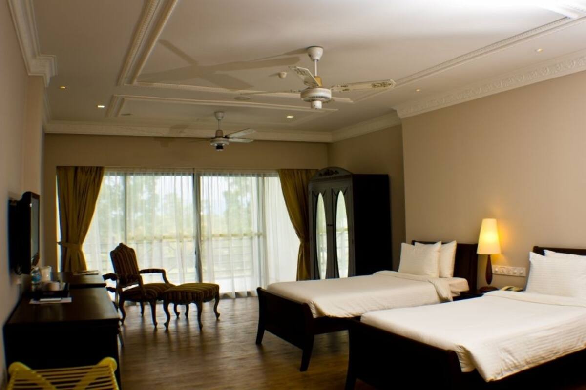 Een hotelkamer met twee bedden, een bureau, een stoel en een groot raam met gordijnen.