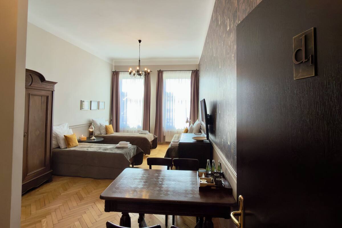 A hotel room with a bed, a desk, a chair, a chandelier, and a large window with curtains.