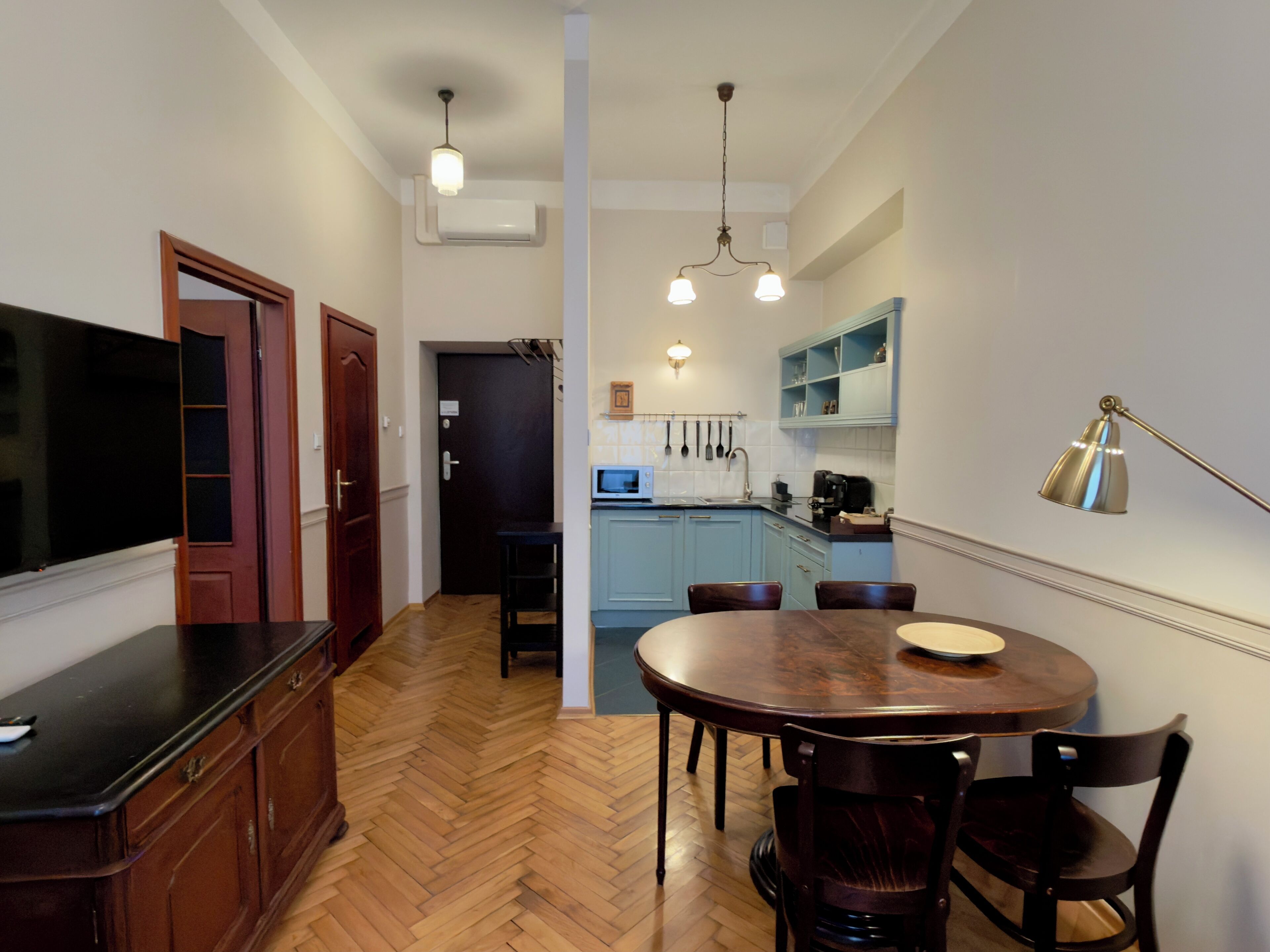 A kitchen with wooden cabinets, a dining table with chairs, a TV, and a microwave.