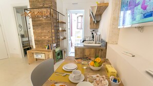 A dining area with a wooden table set for two, a bowl of fruit, and a plate of pastries. - Dione Apartments Ortigia (Syracuse)