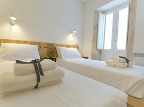 A hotel room with two beds, each with white linens and pillows, a wooden headboard, and a window with white shutters.