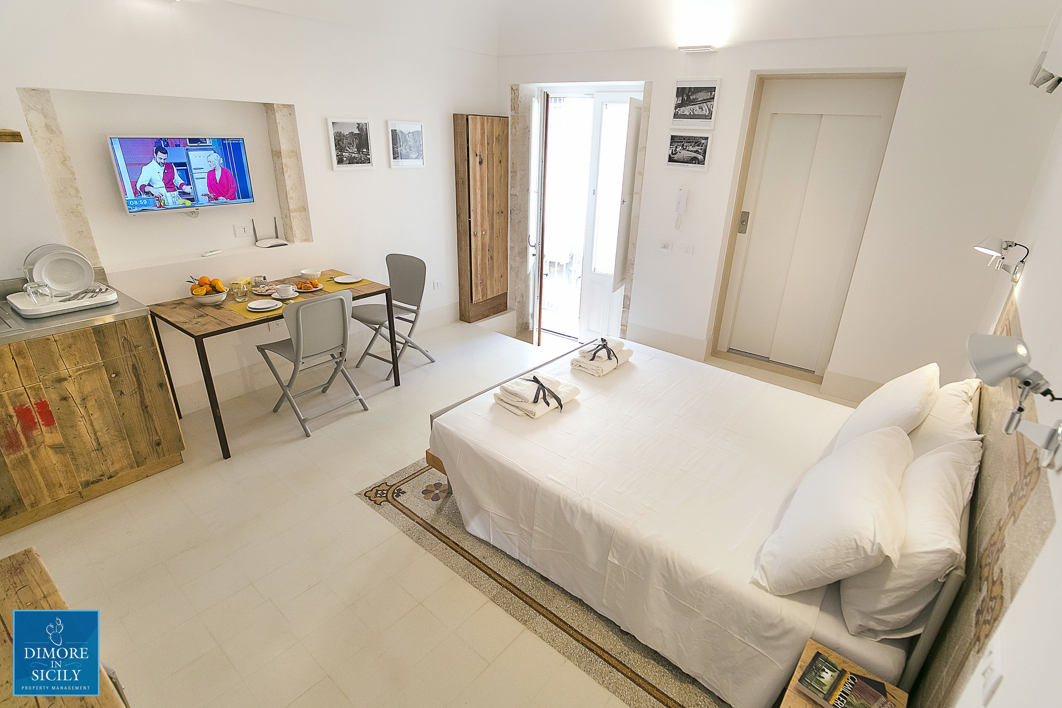 A hotel room with a bed, a desk with a chair, a television, and a wardrobe.