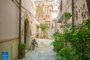 Un estrecho callejón adoquinado con una bicicleta estacionada a la izquierda, rodeado de abundante vegetación y arquitectura tradicional.