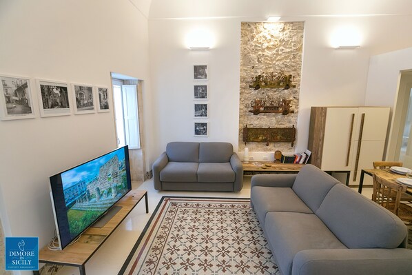 A living room with a flat-screen TV, grey sofas, a patterned rug, and framed pictures on the wall.