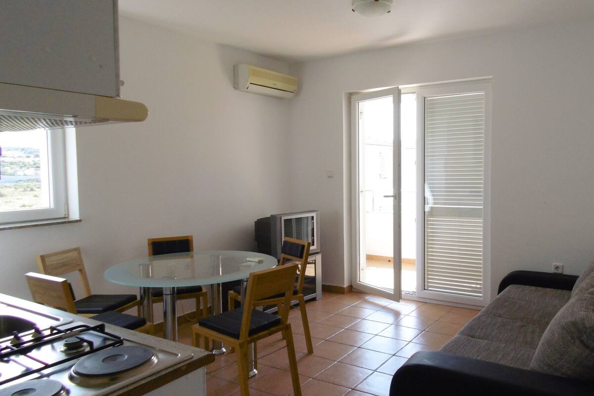 A compact living space with a dining table, chairs, a sofa, a TV, and a kitchen area with a stove.