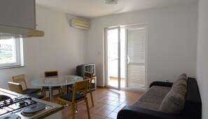 A compact living space with a dining table, chairs, a sofa, a TV, and a kitchen area with a stove.
