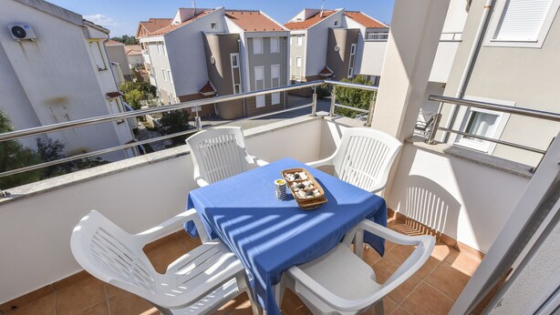 Ein Balkon mit Tisch und Stühlen, einer Snack-Korb und Blick auf angrenzende Gebäude.