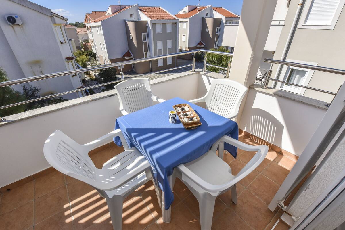 A balcony with a table and chairs, a basket of snacks, and a view of neighboring buildings.