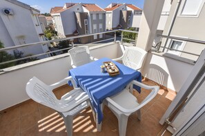 Een balkon met een tafel en stoelen, een mand met snacks en uitzicht op omliggende gebouwen.
