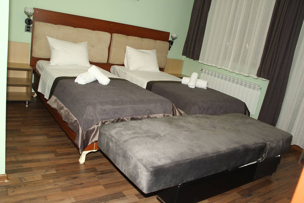 A hotel room with two beds, a wooden floor, and a radiator.