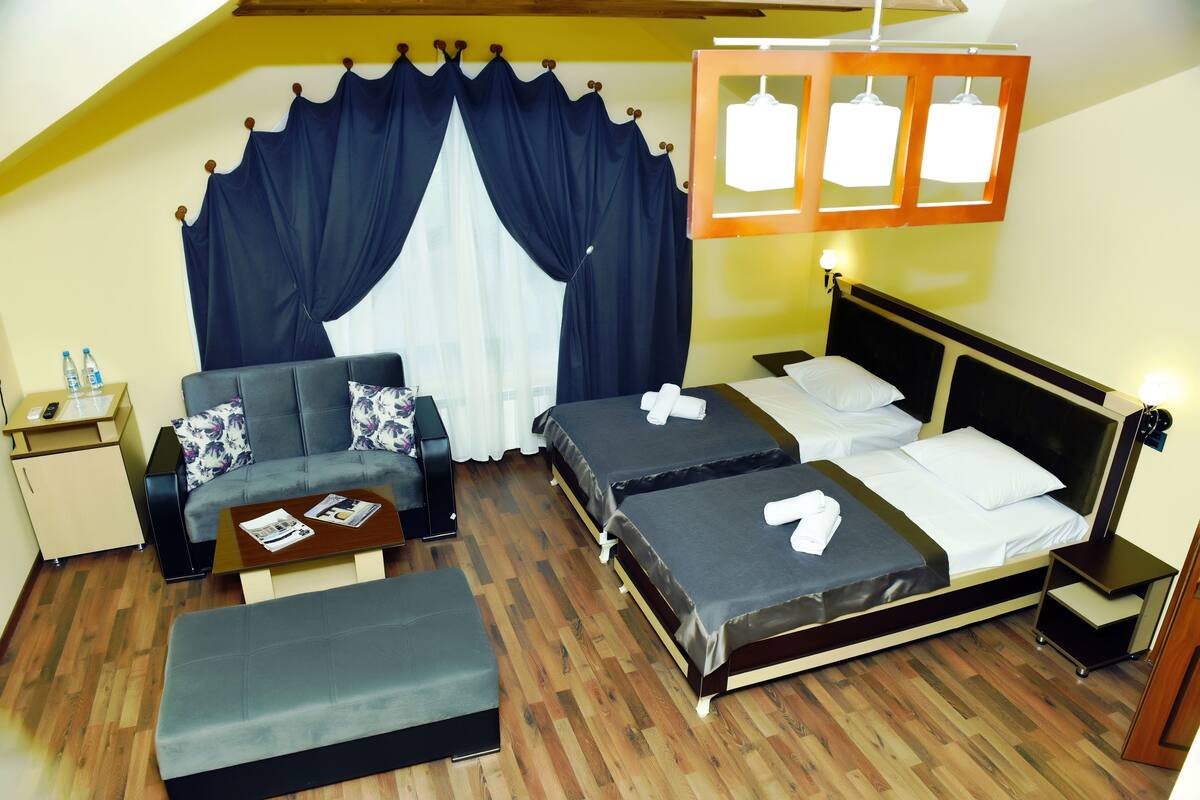 A hotel room with a sofa, two single beds, a small table, and a bench.