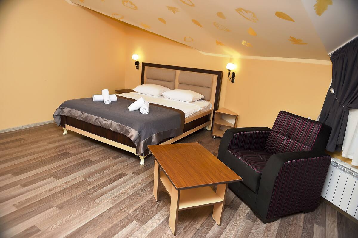 A hotel room with a bed, bedside table, chair, and a radiator.