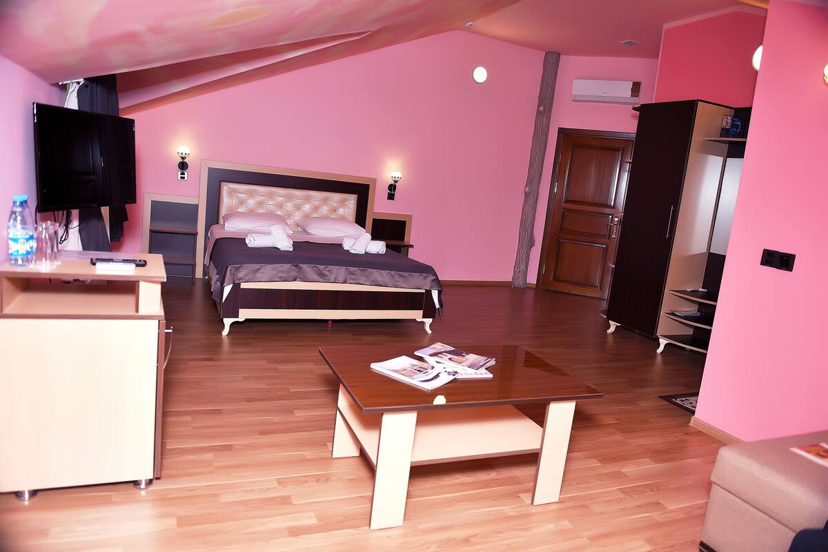 A bedroom with a bed, bedside tables, a TV, a desk, and a wardrobe.