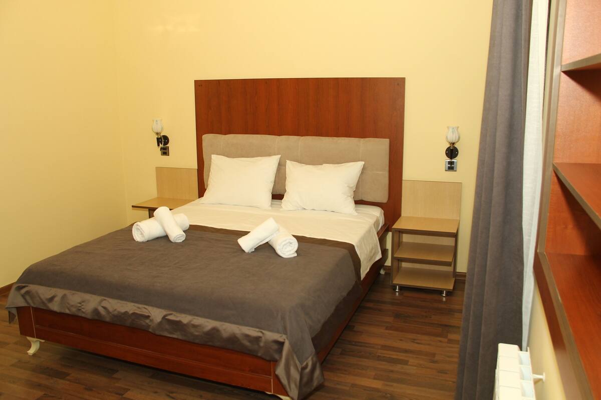 A neatly made bed with a brown bedspread and white pillows, two bedside tables with lamps, and a wooden headboard.