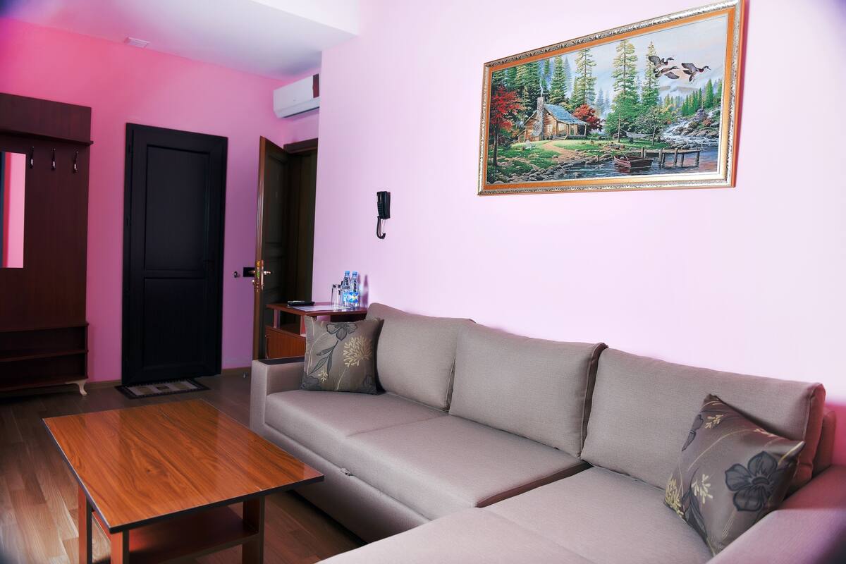 A living room with a sofa, a wooden coffee table, a painting on the wall, and a door.