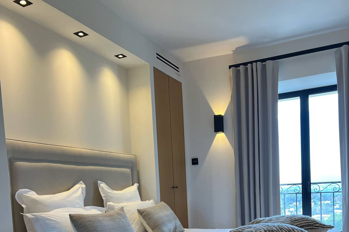 Quarto moderno com uma cama grande, uma mesinha de cabeceira e vista para o exterior.
