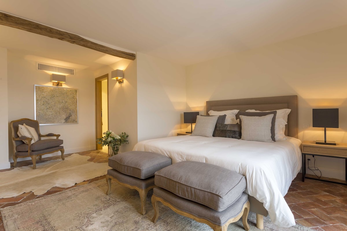 Quarto com cama grande, duas mesas de cabeceira, uma cadeira e um tapete.