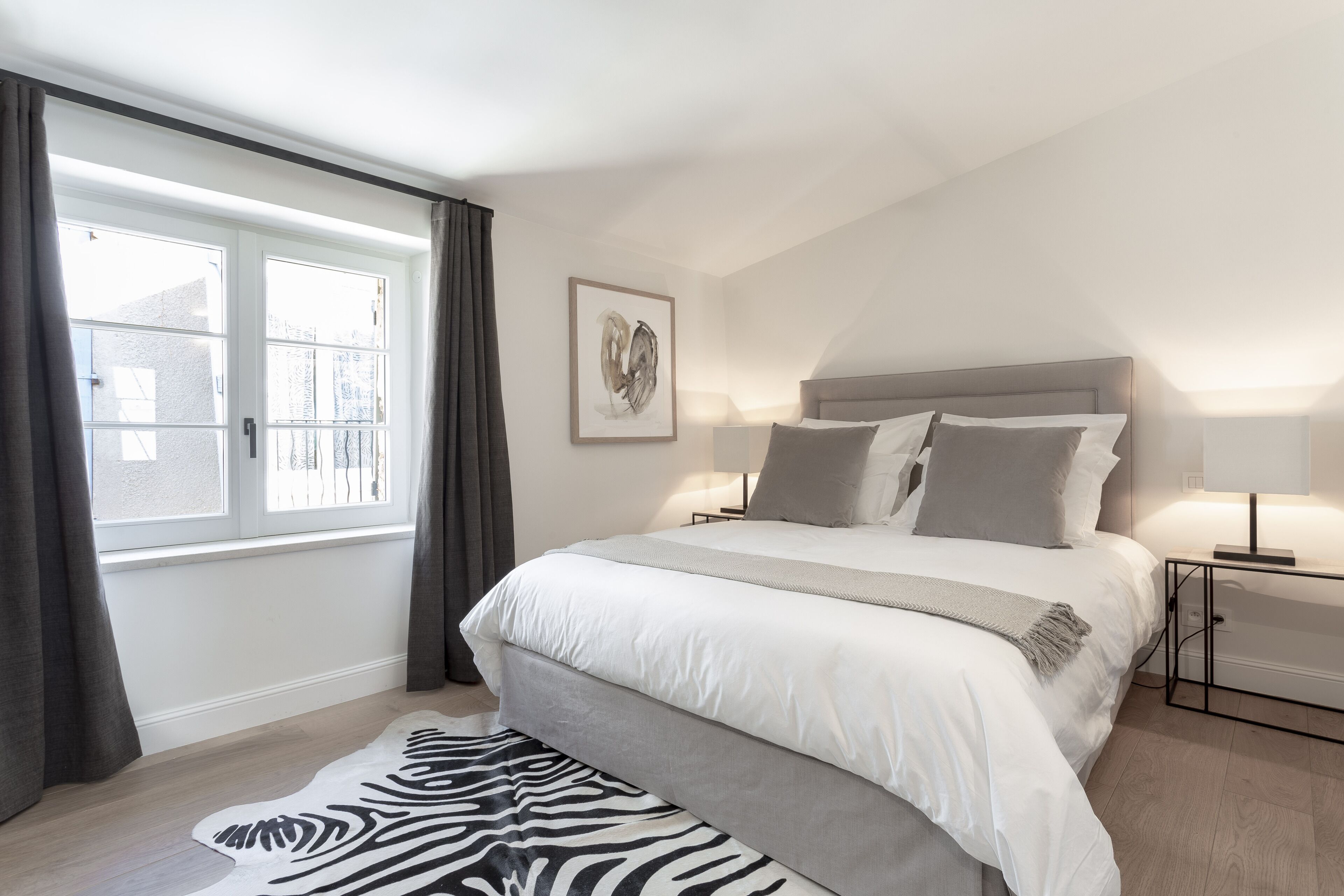 Une chambre avec un grand lit, un tapis à motifs zébrés, une fenêtre avec des rideaux et une œuvre d’art encadrée accrochée au mur.
