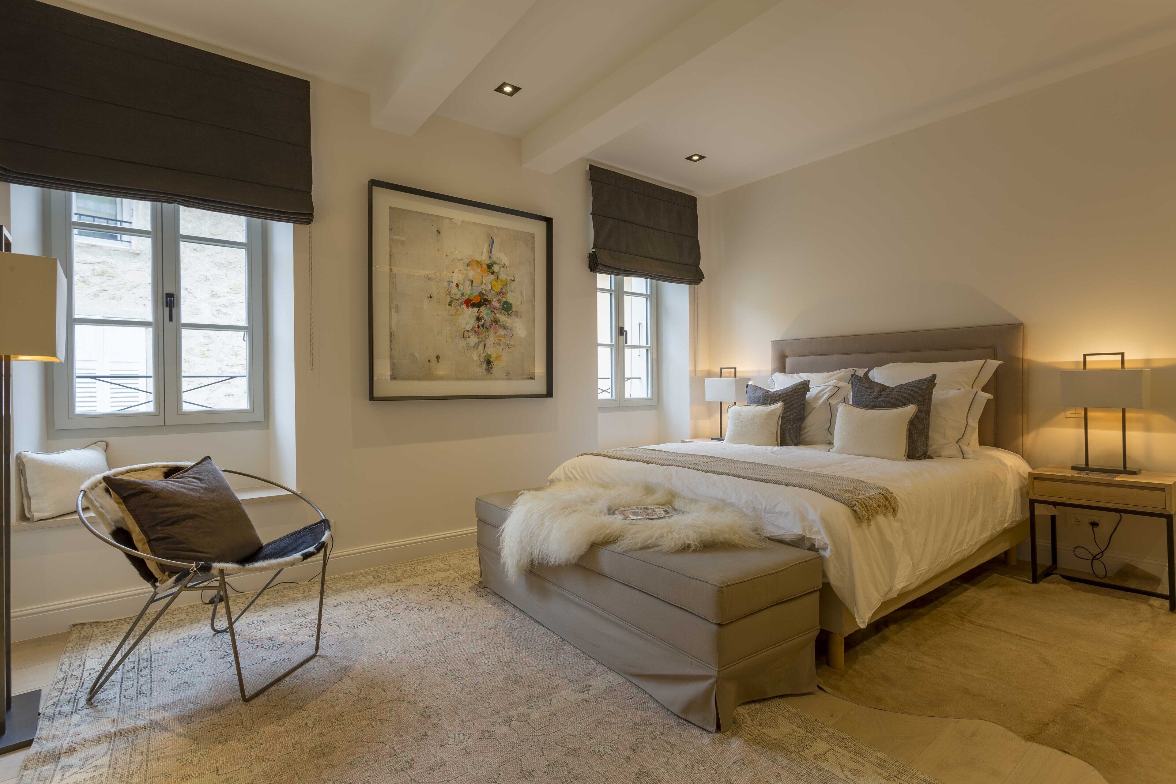 Een slaapkamer met een groot bed, een stoel, een bankje en een schilderij aan de muur.