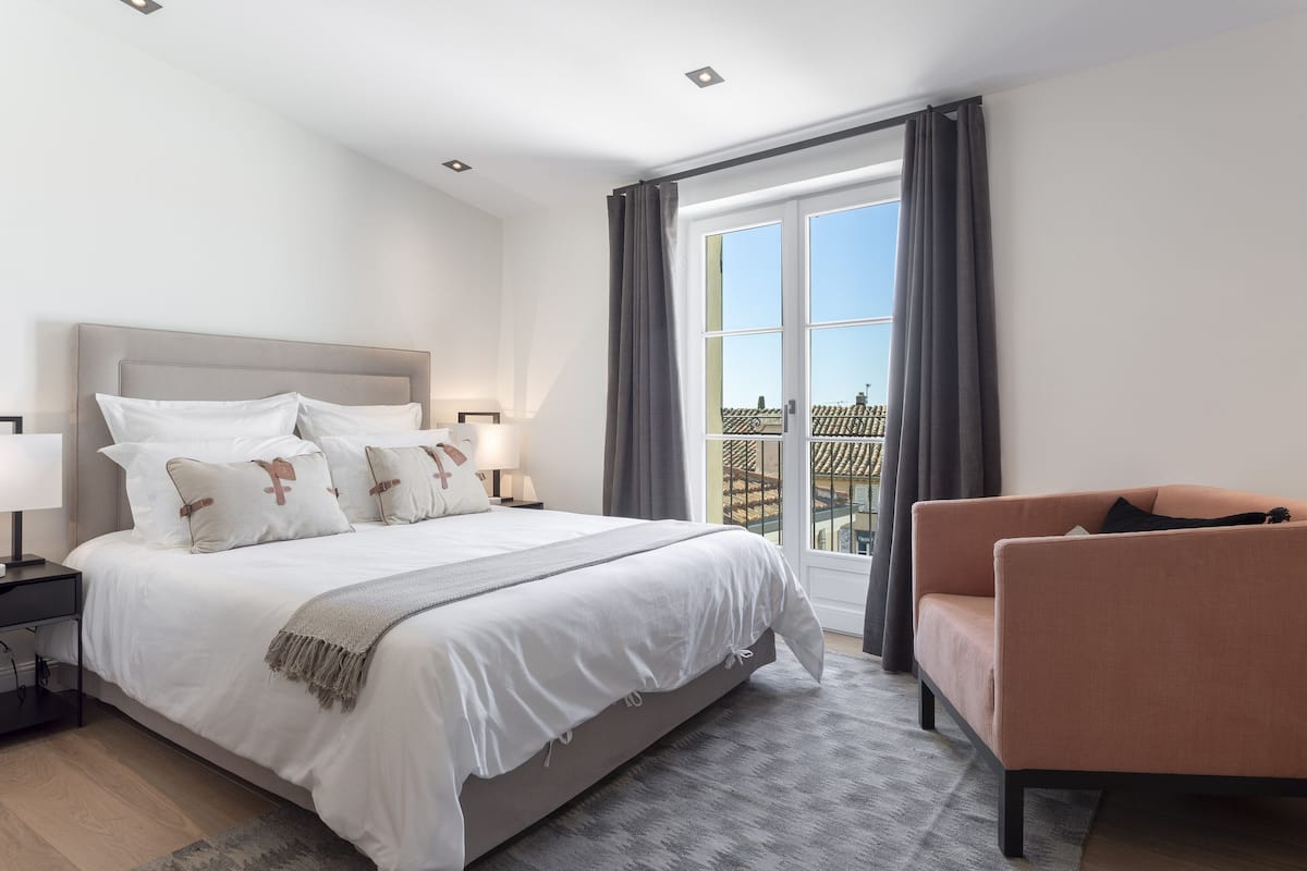 Quarto moderno com uma cama grande, um sofá, uma mesinha de cabeceira e uma janela com cortinas.