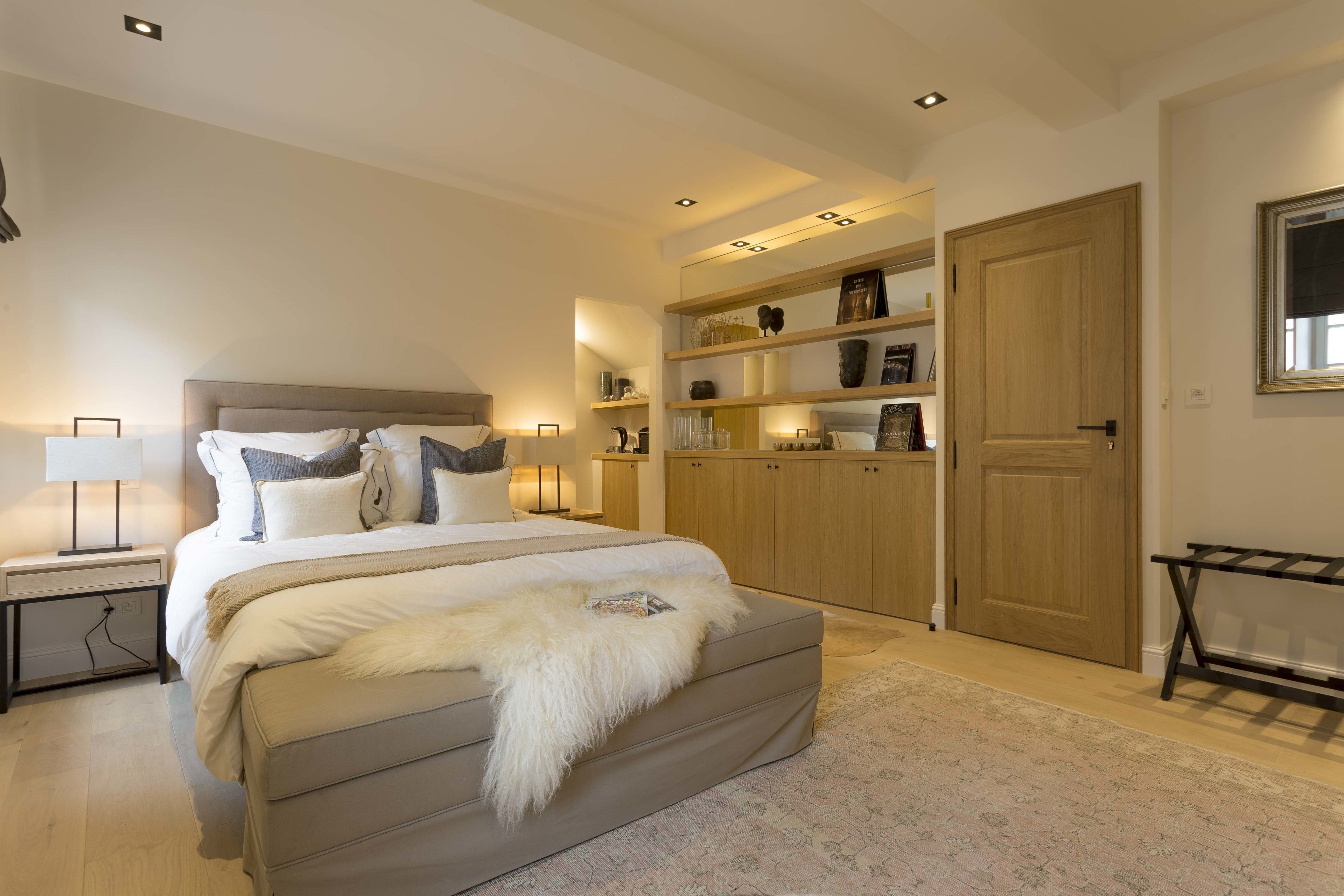 Une chambre à coucher avec un grand lit, des tables de chevet, une armoire et des étagères intégrées ornées d’objets décoratifs.