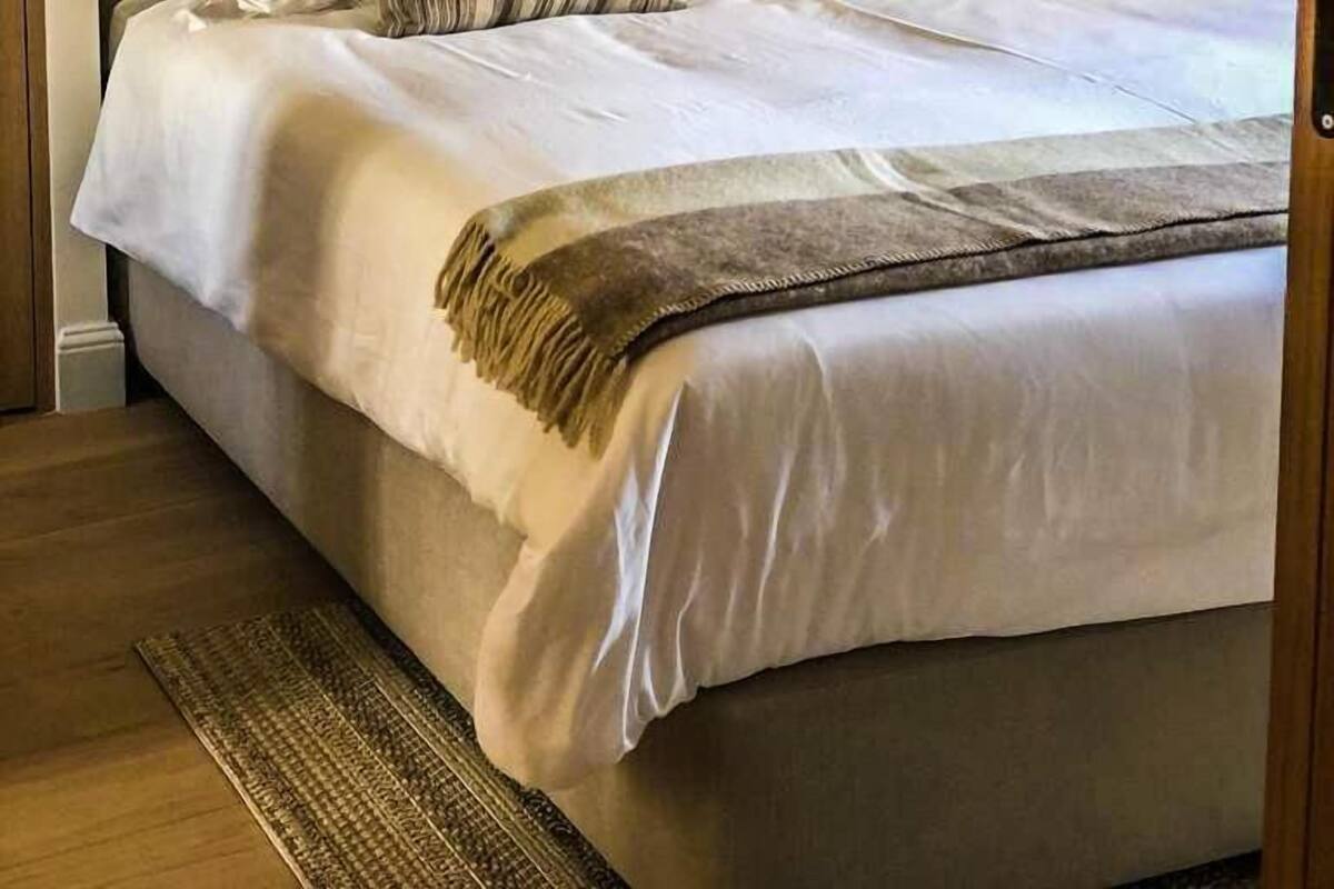 Uma cama com roupa de cama branca, almofadas listradas e um cobertor.