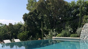 A clear swimming pool with a tiled edge, surrounded by lush greenery and a stone wall. - Mougins Luxury Retreats (Mougins)