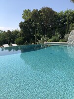 Una piscina cristalina con borde de baldosas, rodeada de exuberante vegetación y un muro de piedra.